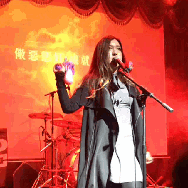 a woman singing into a microphone with chinese writing on the back wall behind her