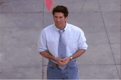 a man in a blue shirt and tie stands on a sidewalk .