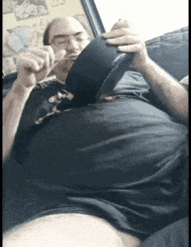 a man with a very large belly is sitting on a couch eating something