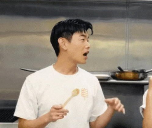 a man in a white t-shirt is holding a wooden spoon in his hand .