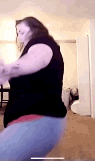a woman in a black shirt and blue jeans is dancing in a living room