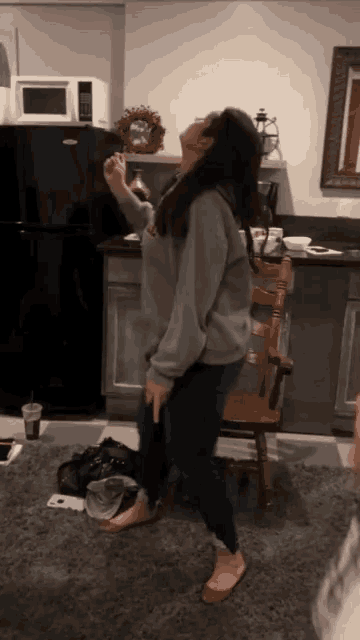 a woman in a grey sweatshirt is standing in front of a black refrigerator