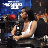 a woman is sitting at a table with a microphone in front of a sign that says breakfast club