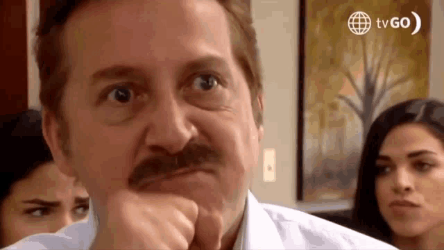 a man with a mustache is making a funny face with his hand on his chin .