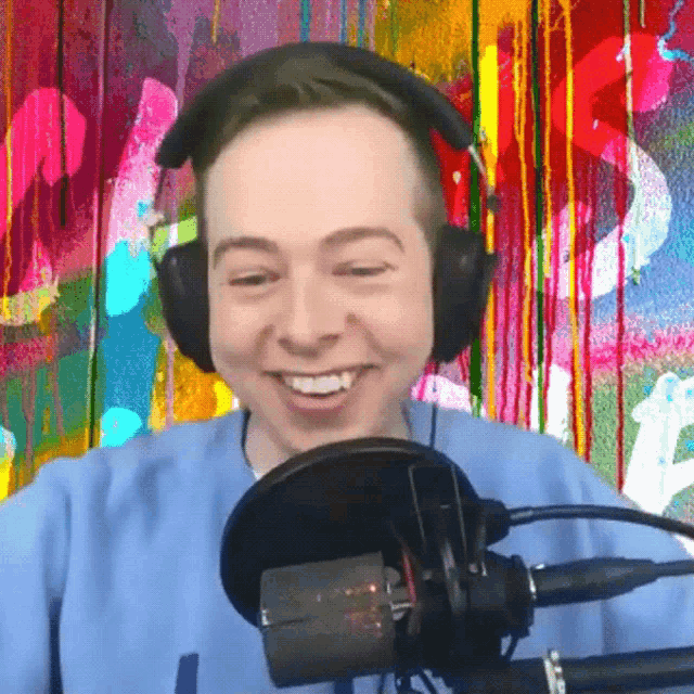 a man wearing headphones is smiling in front of a colorful wall