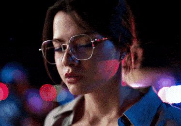 a woman wearing glasses and a blue shirt is looking down with her eyes closed