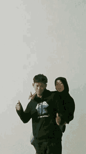 a man in a black hoodie holds a woman on his back and gives a thumbs up
