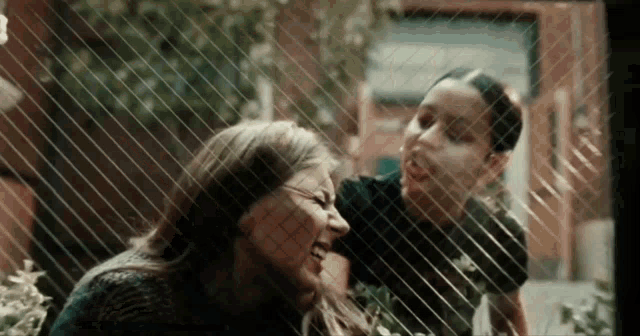 two women are laughing in front of a window with a fence in the background .