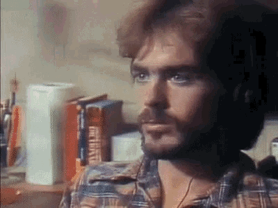 a man in a plaid shirt is sitting in front of a stack of books including one that says ' the bible '