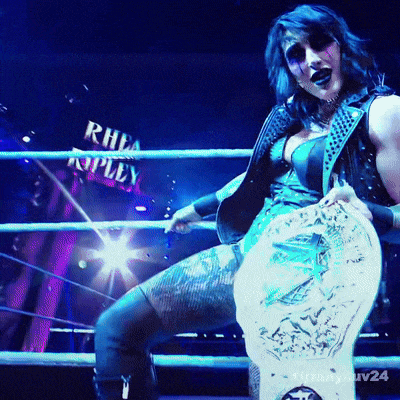 a woman in a wrestling ring with the name rhea ripley on the wall in the background