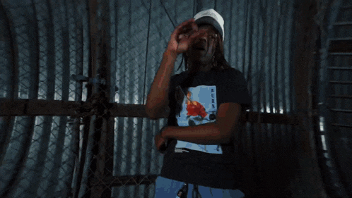 a man standing in front of a chain link fence wearing a black t-shirt with a picture of a bird on it