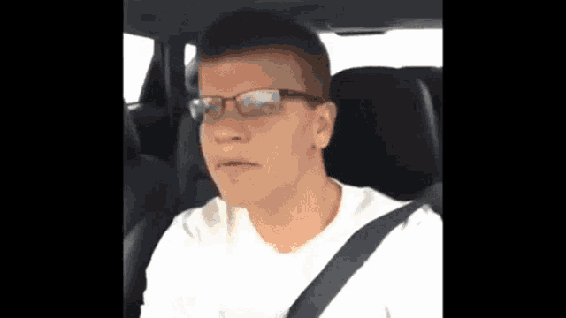 a man wearing glasses is sitting in a car with a seat belt .