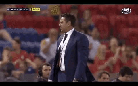 a man in a suit and tie is standing in front of a crowd during a soccer game .