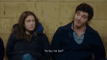 a man and a woman are sitting next to each other against a wall .