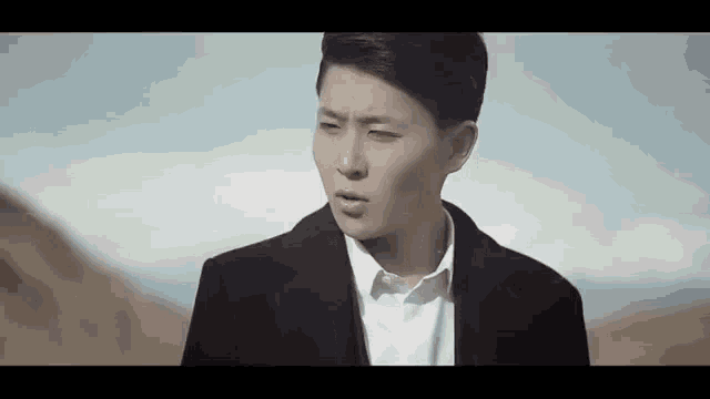 a man in a suit and white shirt is standing in the desert .