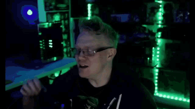 a man wearing glasses is giving the ok sign in a dark room with green lights .