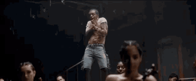 a man is singing into a microphone while standing on a rope in front of a group of dancers .