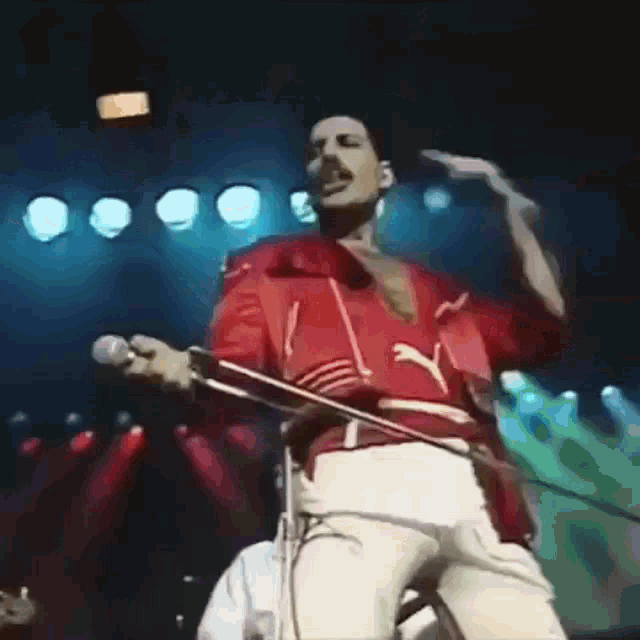 a man in a red shirt is singing into a microphone on stage .