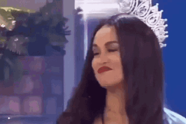 a woman with long dark hair is wearing a crown on her head and making a funny face .