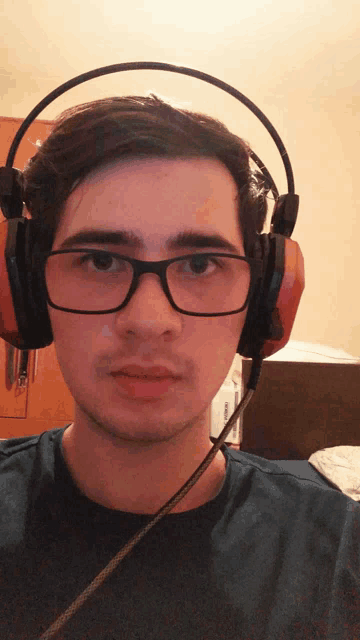 a young man wearing headphones and glasses looks at the camera