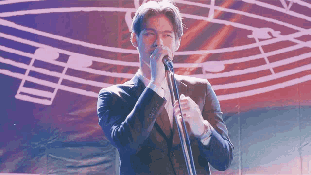 a man in a suit sings into a microphone in front of music notes