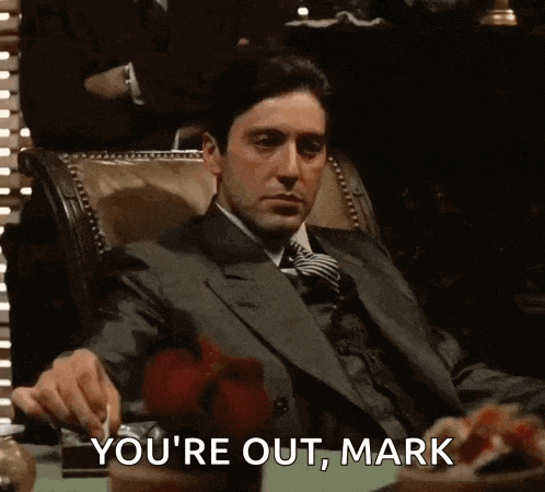 a man in a suit and tie is sitting in a chair and saying you 're out mark .