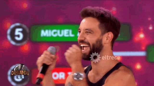 a man with a beard is singing into a microphone with the name miguel behind him