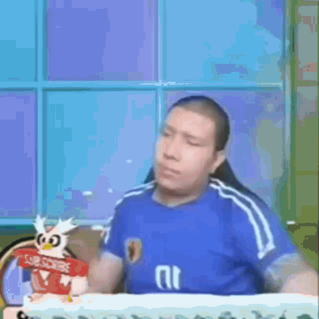 a man in a blue shirt is sitting at a desk with an owl holding a sign that says subscribe