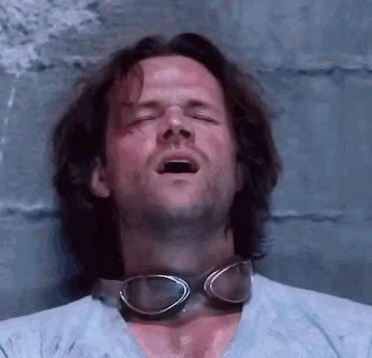 a man wearing goggles around his neck is laying down with his eyes closed and his mouth open .