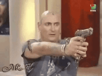 a bald man is holding a gun in front of a red curtain and a sign that says vivo .