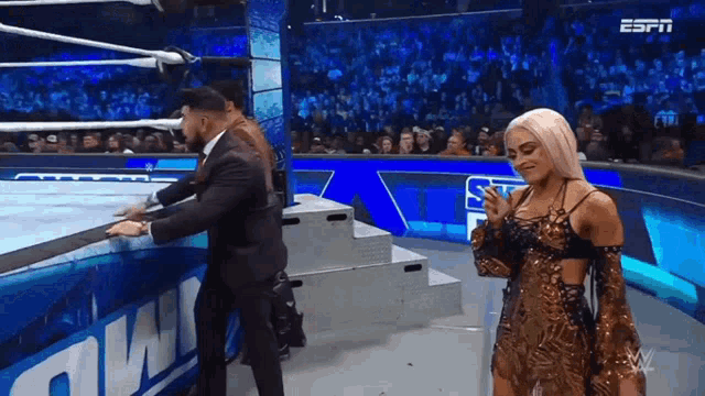 a woman in a dress is standing in a wrestling ring with a man in a suit behind her .
