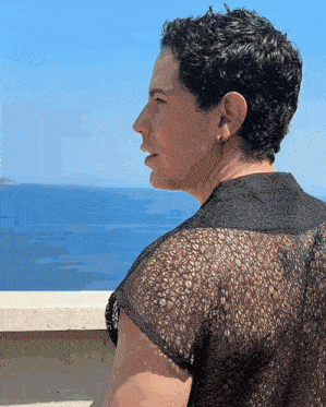 a woman in a black lace top is looking at the ocean