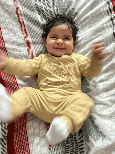 a baby is laying on a bed wearing a yellow shirt with a bear on it