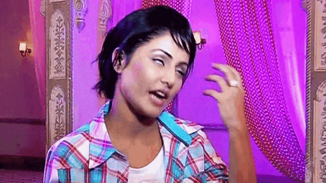 a woman in a plaid shirt is making a funny face while standing in front of a purple curtain .