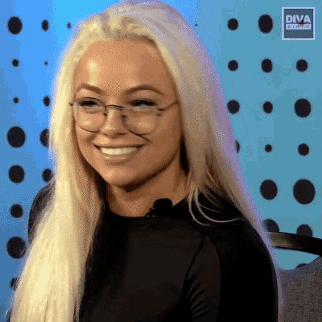 a blonde woman wearing glasses and a black shirt is smiling and looking at the camera .