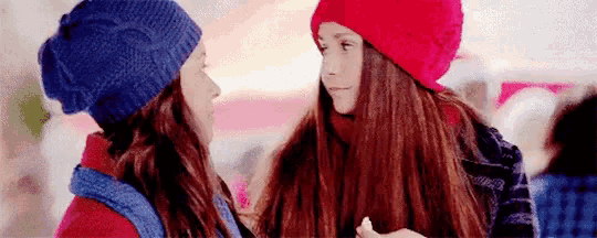 two girls wearing hats are looking at each other in a crowded area .