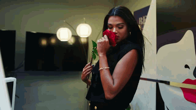 a woman smells a red rose in front of a wall that says ' be '