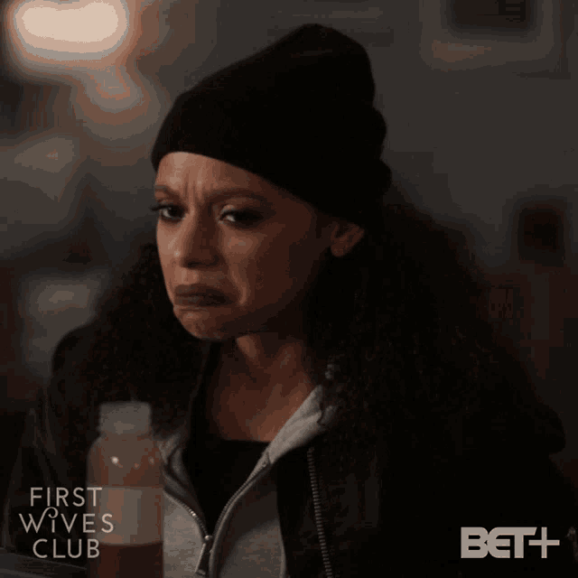 a woman in a black beanie is holding a bottle of juice from the first wives club