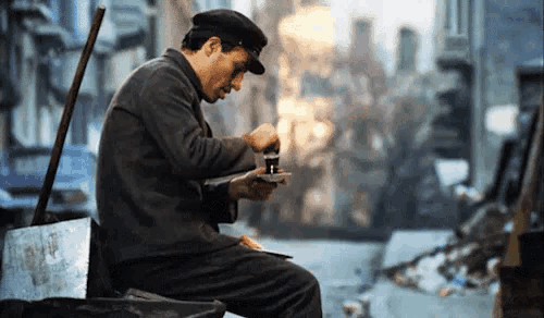 a man wearing a hat is sitting on a trash can looking at his phone