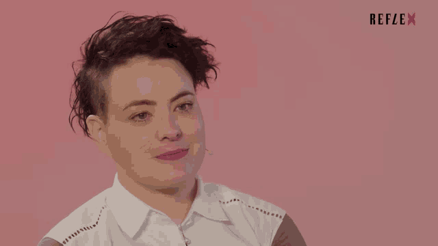 a woman with short hair is smiling in front of a pink background with reflex written in red