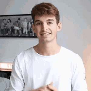 a young man is wearing a white shirt and smiling in front of a picture on the wall .