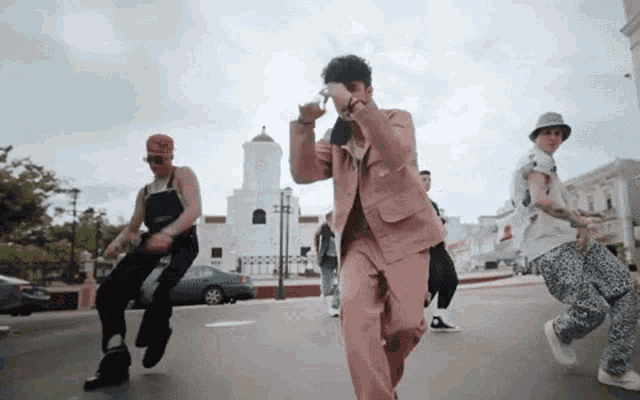 a group of men are dancing on a street in front of a white building