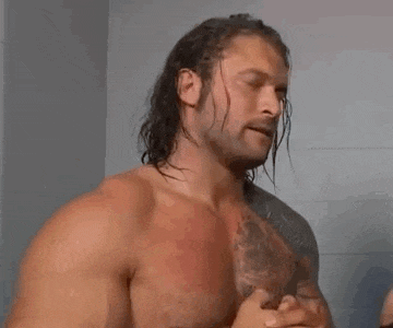 a shirtless wrestler with long hair and a beard is standing in a bathroom .