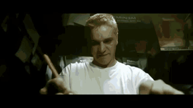 a man in a white shirt is holding a pencil in his mouth and looking at the camera .
