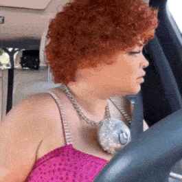 a woman with red curly hair wearing a pink top and necklace