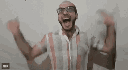 a man wearing glasses and a striped shirt is raising his arms in the air .