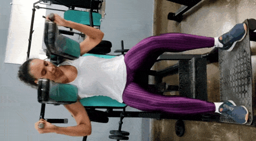 a woman in purple pants is laying down on a machine