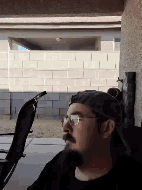 a man with a beard wearing glasses and a hat is sitting in front of a brick wall