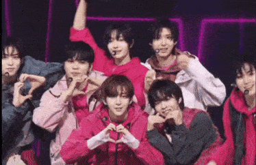 a group of young men are standing next to each other on a stage making heart shapes with their hands .