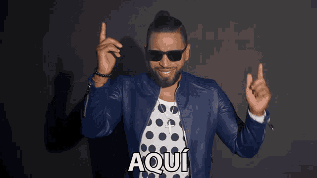 a man wearing sunglasses and a polka dot shirt has the word aqui on his chest